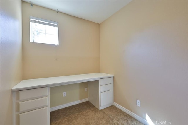 unfurnished office featuring light carpet, built in desk, and baseboards