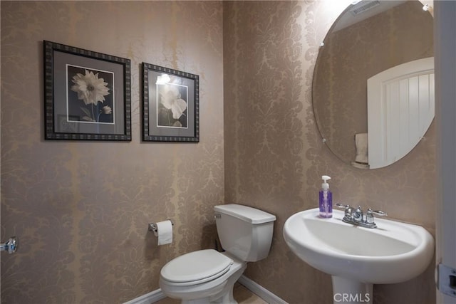 bathroom with toilet, wallpapered walls, visible vents, and baseboards