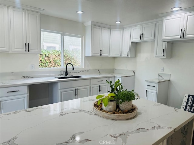 kitchen with recessed lighting, white cabinets, light stone countertops, and a sink