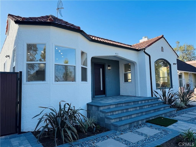 mediterranean / spanish home with stucco siding, fence, a porch, and a tile roof