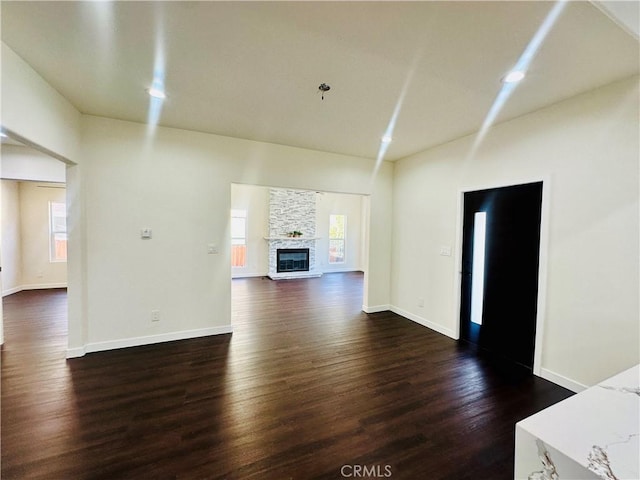 unfurnished living room featuring a stone fireplace, recessed lighting, baseboards, and dark wood-style flooring