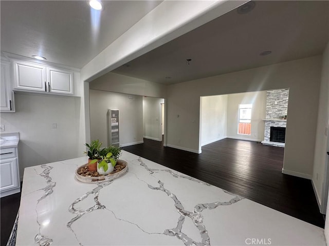 interior space featuring dark wood-type flooring, open floor plan, a stone fireplace, white cabinets, and light stone countertops