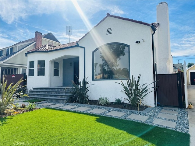 view of front of house featuring a tile roof, stucco siding, a chimney, and a gate