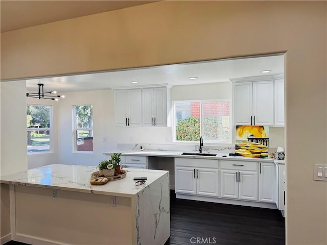 kitchen featuring light stone counters, white cabinets, a wealth of natural light, and a sink