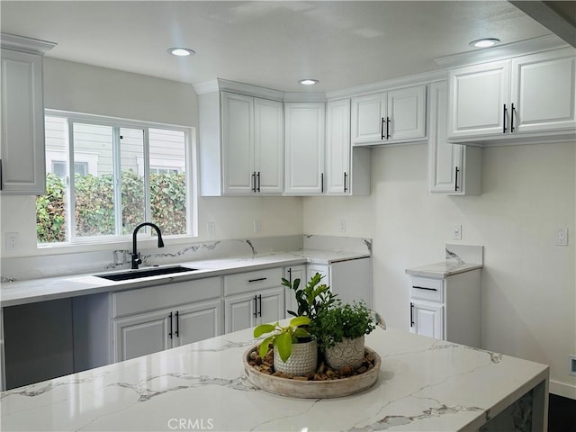 kitchen with light stone counters, recessed lighting, white cabinetry, and a sink