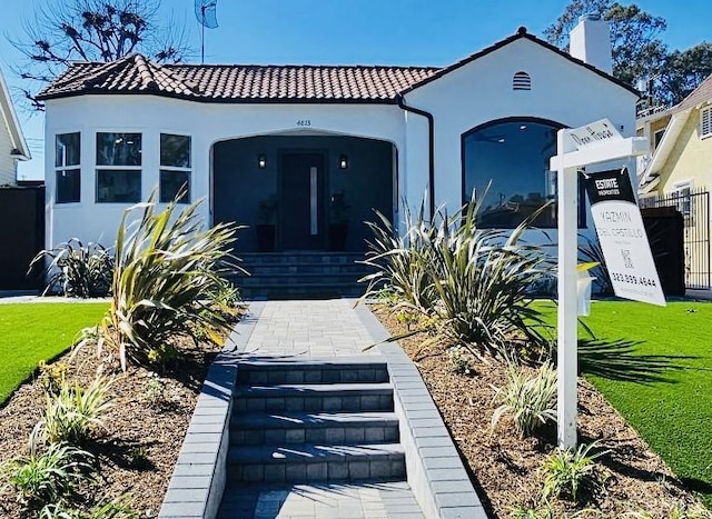 mediterranean / spanish-style home featuring a tile roof, fence, a front lawn, and stucco siding