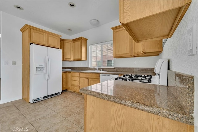 kitchen featuring light tile patterned floors, a peninsula, white appliances, a sink, and dark stone counters