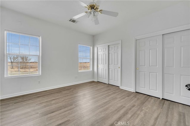 unfurnished bedroom featuring multiple windows, wood finished floors, visible vents, and multiple closets