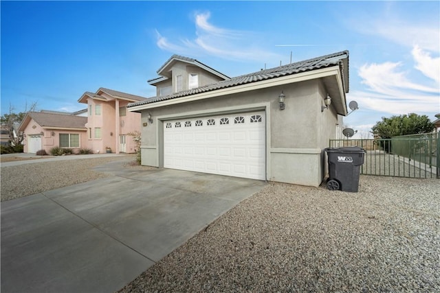 view of front of house featuring a garage, concrete driveway, a tile roof, fence, and stucco siding