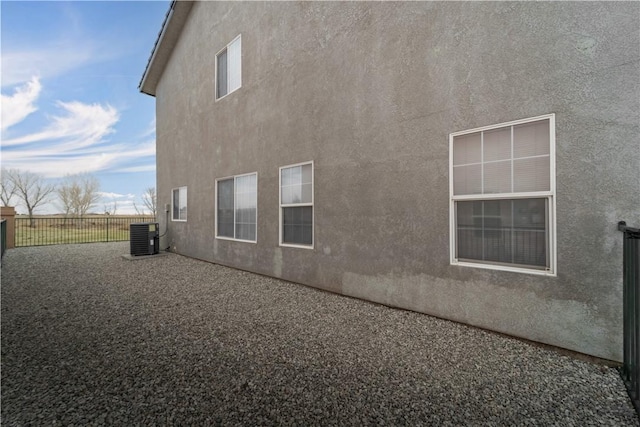 view of property exterior with fence, central AC, and stucco siding