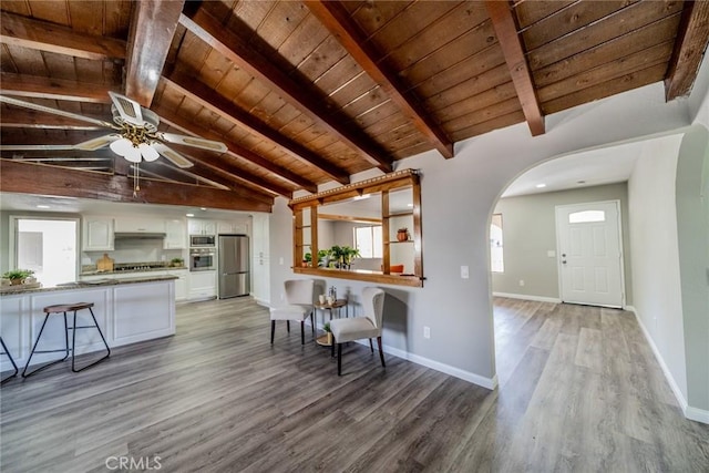 kitchen with arched walkways, vaulted ceiling with beams, wood ceiling, white cabinets, and appliances with stainless steel finishes