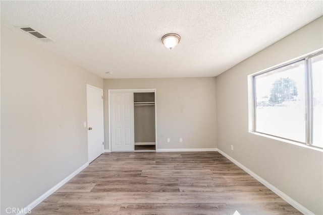 unfurnished bedroom featuring baseboards, visible vents, a closet, and wood finished floors