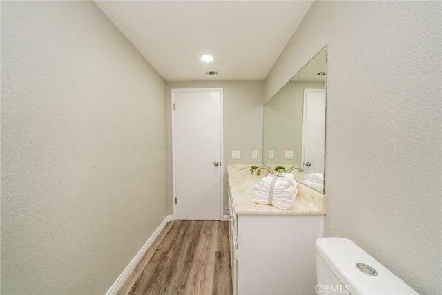 bathroom with baseboards, visible vents, toilet, wood finished floors, and vanity