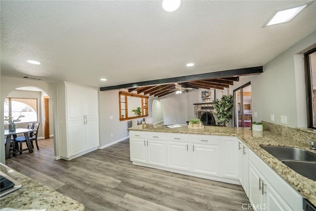 kitchen with light wood finished floors, arched walkways, a peninsula, a textured ceiling, and a sink