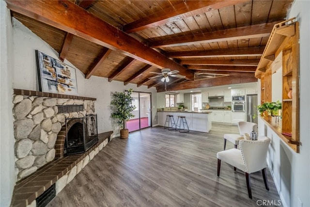 unfurnished living room featuring vaulted ceiling with beams, ceiling fan, wooden ceiling, a fireplace, and wood finished floors