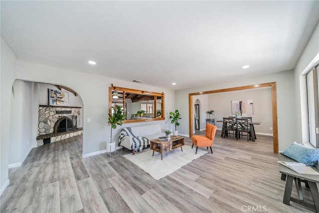 living area with light wood-style floors, visible vents, a stone fireplace, and baseboards