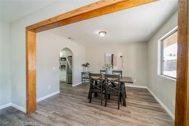 dining space featuring arched walkways, baseboards, and wood finished floors