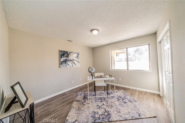 office with visible vents, a textured ceiling, baseboards, and wood finished floors