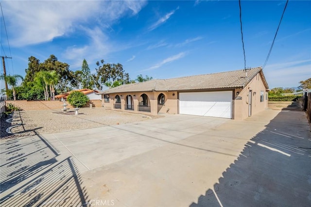 ranch-style home featuring a tile roof, stucco siding, fence, a garage, and driveway