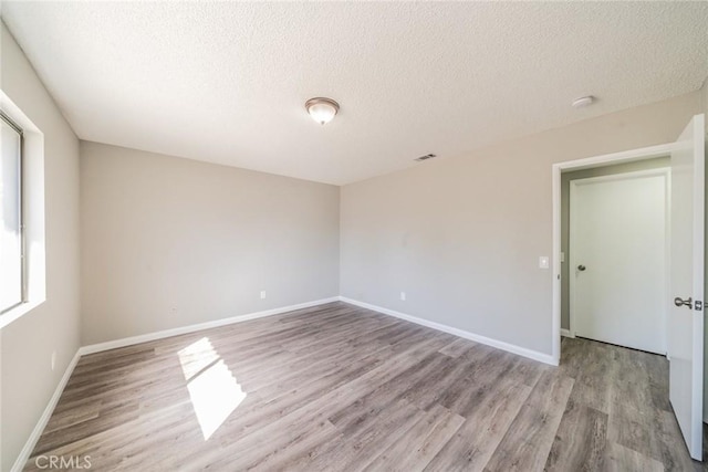 empty room with baseboards, light wood-style flooring, visible vents, and a textured ceiling