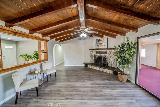 living area featuring arched walkways, wooden ceiling, a stone fireplace, and wood finished floors