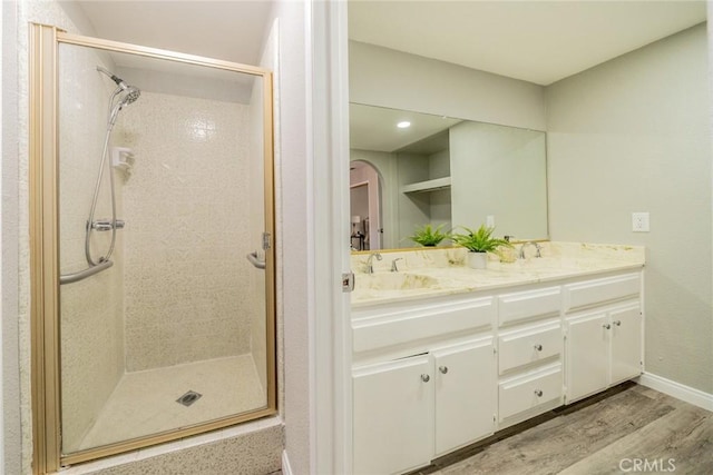 full bath with a sink, wood finished floors, baseboards, a shower stall, and double vanity