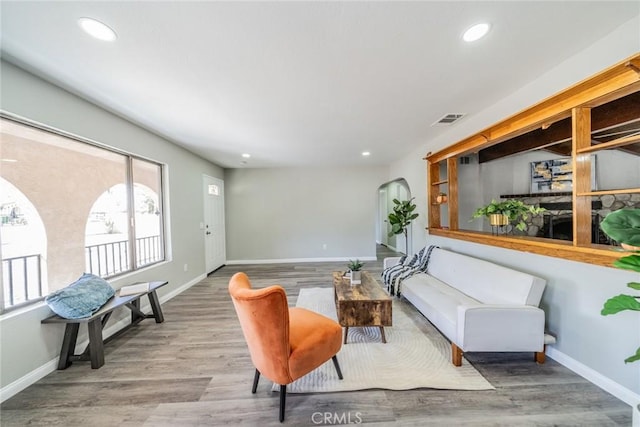 living area featuring baseboards, visible vents, arched walkways, wood finished floors, and recessed lighting