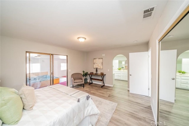 bedroom featuring arched walkways, light wood finished floors, visible vents, and baseboards