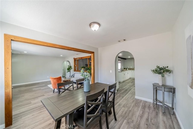 dining room with light wood finished floors, baseboards, and arched walkways