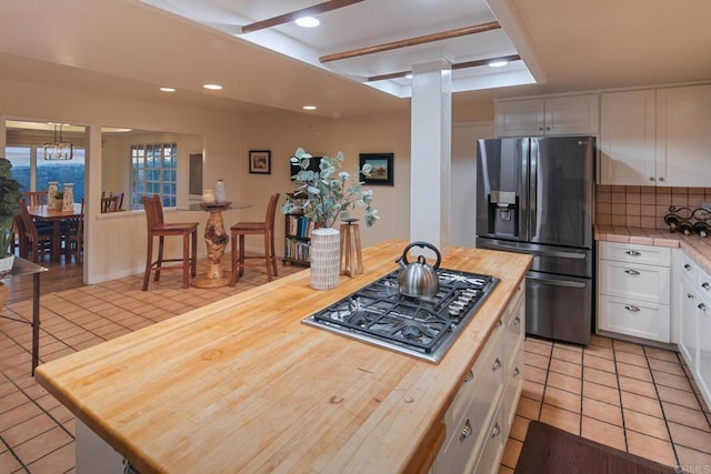 kitchen featuring stainless steel gas cooktop, wooden counters, light tile patterned flooring, and refrigerator with ice dispenser