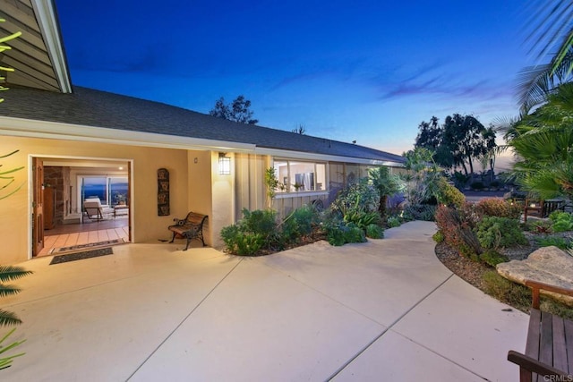 exterior space with a patio area, roof with shingles, and stucco siding