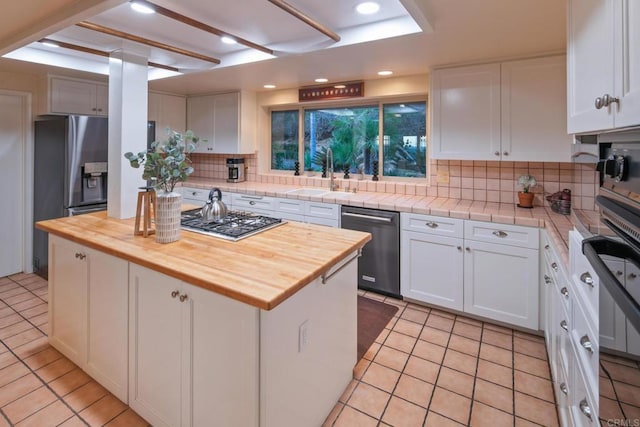 kitchen featuring stainless steel gas stovetop, wooden counters, white cabinetry, a sink, and dishwashing machine