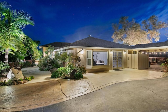 back of house at twilight with french doors, a shingled roof, and stucco siding