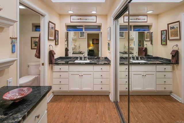 full bathroom featuring a skylight, two vanities, toilet, a sink, and wood finished floors