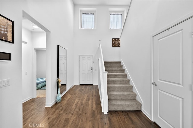 staircase with a high ceiling, wood finished floors, and baseboards