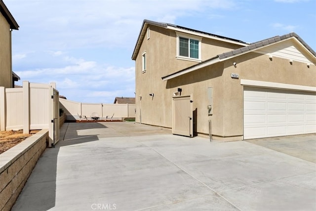 view of home's exterior with concrete driveway, an attached garage, fence, and stucco siding