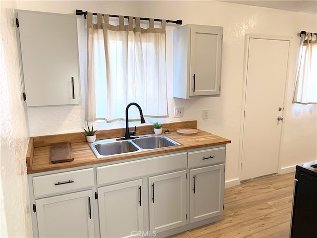 kitchen featuring a textured wall, butcher block counters, a sink, light wood-style floors, and black electric range oven