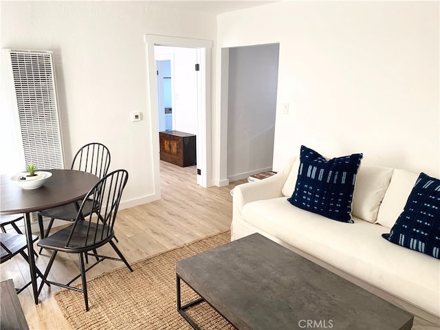 living room with a heating unit, baseboards, and light wood finished floors