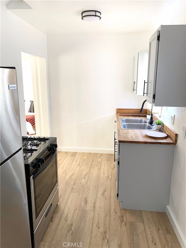 kitchen featuring light wood-style flooring, wood counters, gray cabinets, stainless steel appliances, and a sink