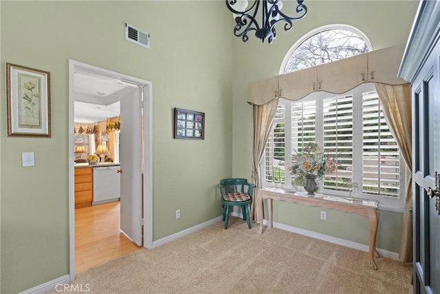 living area with visible vents, a towering ceiling, an inviting chandelier, light carpet, and baseboards