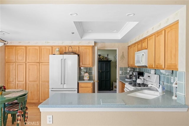 kitchen featuring a tray ceiling, crown molding, light wood finished floors, tasteful backsplash, and white appliances