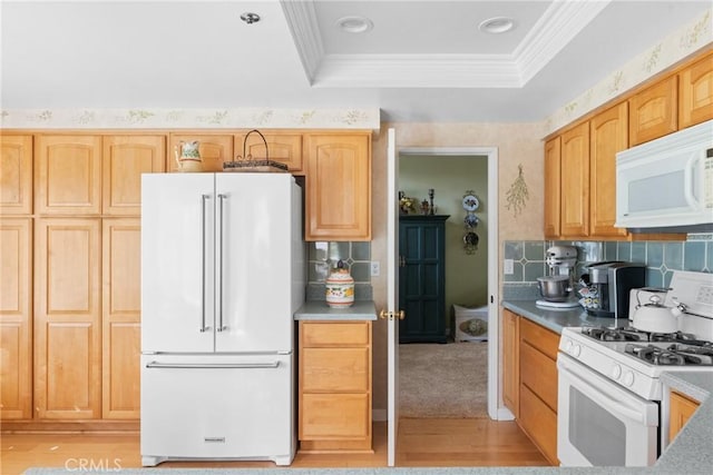 kitchen with a tray ceiling, crown molding, decorative backsplash, light brown cabinetry, and white appliances