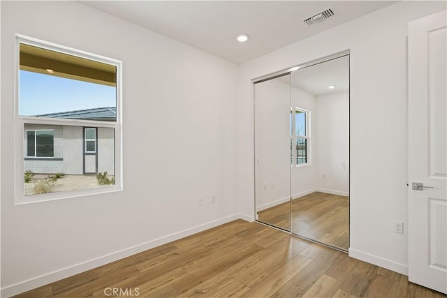 unfurnished bedroom with a closet, multiple windows, wood finished floors, and visible vents