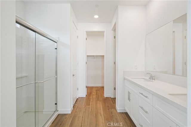 full bath with double vanity, a stall shower, a sink, wood finished floors, and baseboards