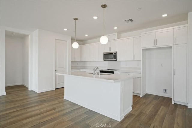 kitchen with visible vents, dark wood finished floors, stainless steel microwave, light countertops, and white cabinetry