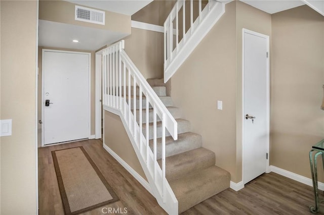 stairway with baseboards, visible vents, and wood finished floors