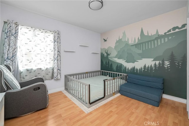 bedroom with a nursery area, wood finished floors, and baseboards