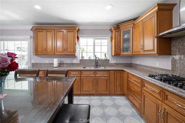 kitchen with a wealth of natural light, wall chimney exhaust hood, brown cabinets, and a sink