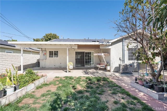 rear view of house featuring a patio, stucco siding, roof mounted solar panels, fence, and cooling unit