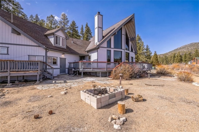 rear view of house featuring a deck, roof with shingles, a chimney, and a fire pit